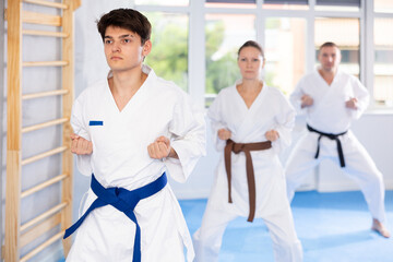 Woman and man in kimono standing in fight stance during group karate training