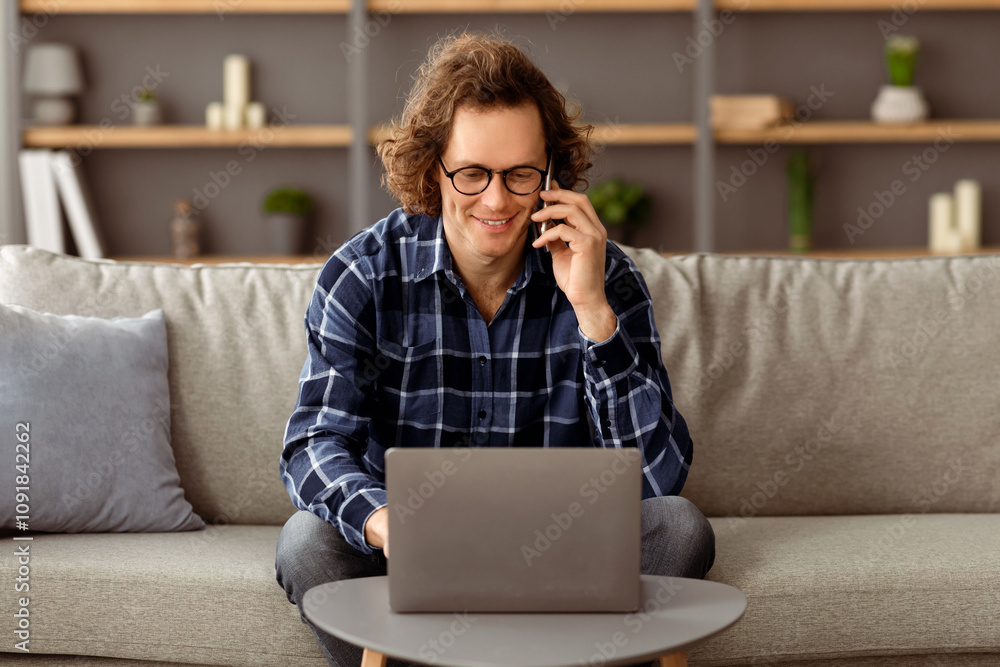 Aufkleber male freelancer talking on mobile phone working on laptop computer sitting on couch at home. long-ha