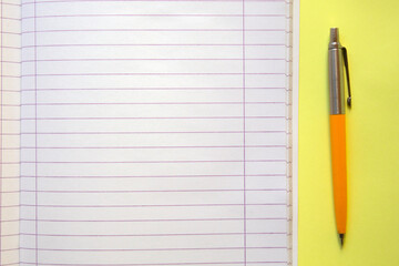 open notebook, with a pen next to , on yellow background. selective focus