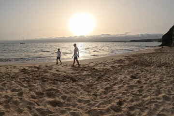 two young friends play football at sunset on a lonely beach with cliffs in the background on a summer day, holidays with friends an family, playing together