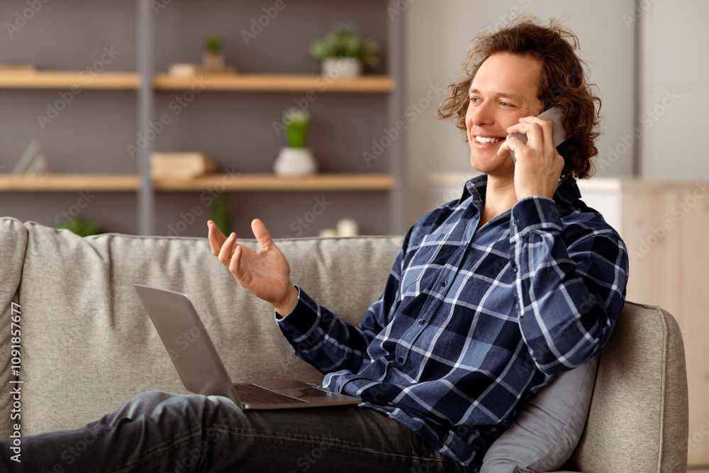 Poster always in touch. cheerful freelancer guy talking on phone sitting with laptop computer on couch at h