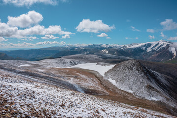 Snowy stony pass, large colorful mountain range and big alpine valley in far away. Snow-white glacier on most beautiful rocky hill in freshly fallen snow among high mountains under clouds in blue sky.