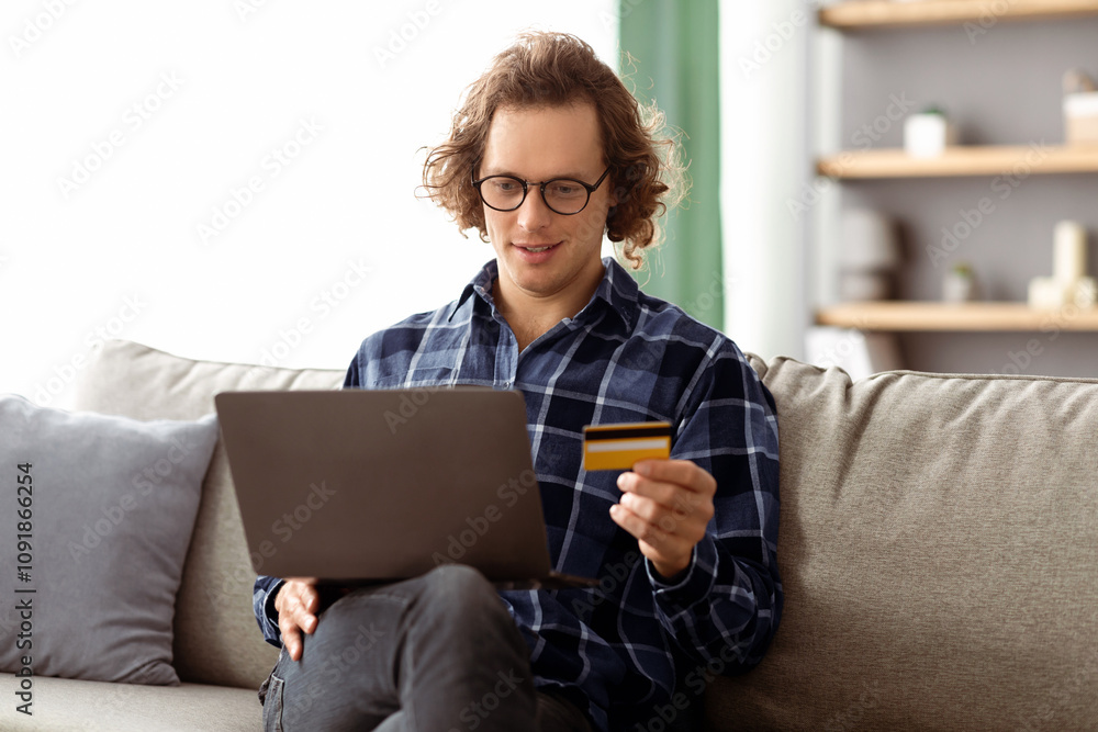 Poster hipster guy using credit card and laptop shopping online sitting on sofa at home. man making payment