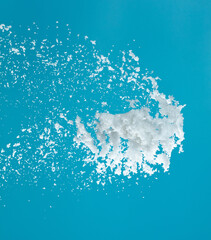 Snow dust element falling over blue sky. Fluffy White snow splash flying or throwing in mid air. Snowfall on blue background isolated