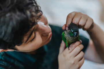 A young girl tenderly holds a vibrant green parrot, showcasing a moment of bonding and affection....