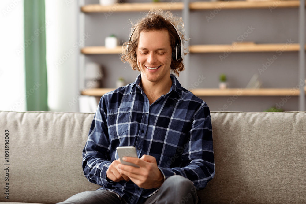 Poster happy man listening to music on phone online enjoying good sound wearing wireless headphones sitting