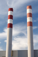 Two white and red chimneys of a factory during the day against the sky.