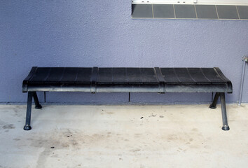 Black bench seat on a concrete surface against a light blue wall