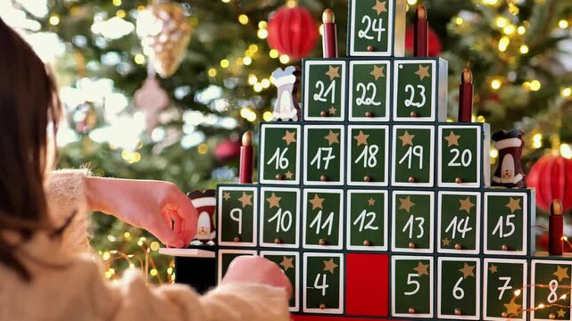 advent calendar. child takes chocolates out of an advent calendar. Wooden Christmas Tree Advent Calendar and a child in a bright, cozy room with a shining Christmas tree.Gifts and surprises for