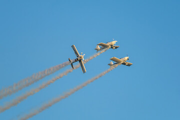 Three stunt aerobatic planes performing stunts in blue sky with smoke trail. Concept of teamwork, collaboration, coordination, trust, precision, difficulty, challenge, speed, synergy