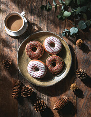 Coffee and donuts on a rustic wooden table with pinecones and eucalyptus leaves, creating a cozy and inviting autumnal scene