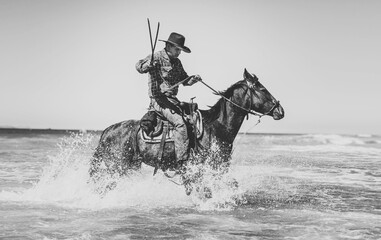 Black and white image of a man riding a horse in the ocean wearing cowboy hat