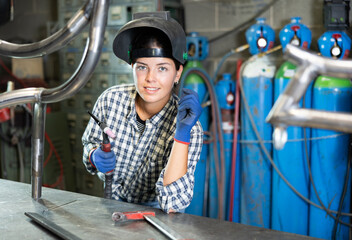 Portrait of a female welder standing with a welding machine and a safety helmet in a metal machining workshop