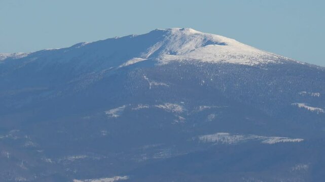 Snow-covered Babia Gora peak in the Beskid Zywiecki range, Poland, rising above the valley under clear winter skies.