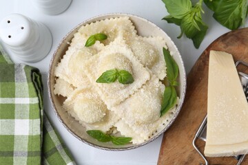 Delicious ravioli with cheese and basil served on white table, flat lay
