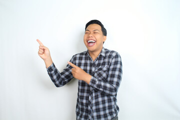 Fototapeta premium carefree asian man pointing hand with laughing expression showing joy and playful emotion wearing casual plaid shirt isolated on white background