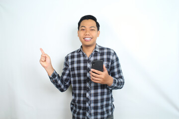 Fototapeta premium smiling asian man pointing to copy space with holding mobile phone isolated on white background