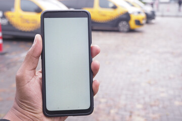 A hand is holding a smartphone that features a blank screen amidst yellow taxis in the background