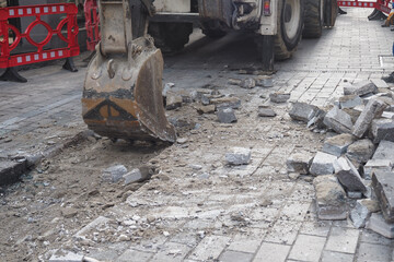 On a construction site, an excavator is actively working on a paved roadway project