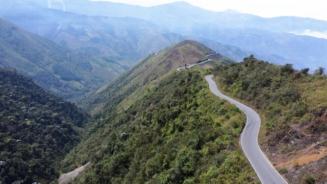 Drone flies along curvy mountain road to summit, surrounded by massive valleys, mountains between Guaranda and Montalvo, Ecuador.