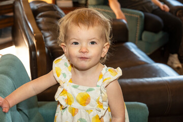 Little girl with a playful expression stands in a cozy living room filled with comfortable furniture