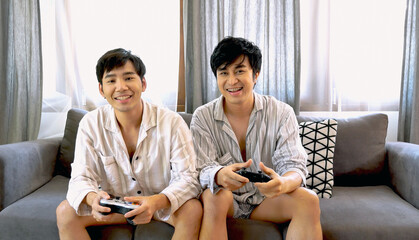 Happy gay couple enjoy playing game together sitting sofa at home living room lifestyle. Friendship...
