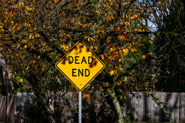 Yellow dead end traffic sign on a sunny fall day with yellow leaves in the background
