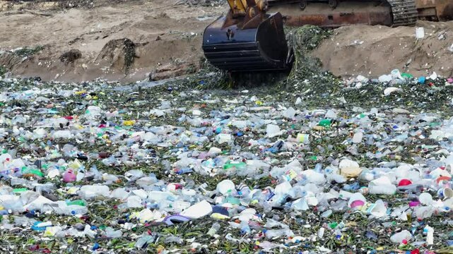 A mechanical excavator cleans up accumulated plastic waste along the seashore in an effort to protect the environment. Ideal footage for sustainability and environmental conservation themes