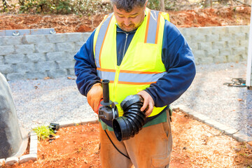 Construction worker wears safety vest as he cuts off part of drainage pipe prior to its installation during construction