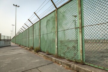 Obraz premium Metal mesh wall with a dirty green tint and rough texture, metal mesh background, grungy look, post-industrial aesthetic, industrial design element, concrete texture