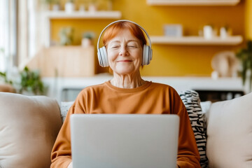 A woman wearing headphones is sitting on a couch and using a laptop. She is smiling and she is enjoying herself