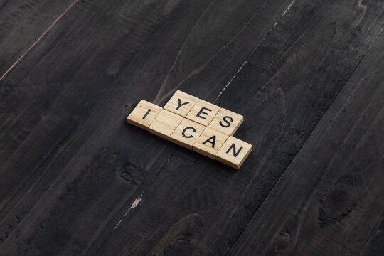Words "YES I CAN" written with letters tiles on wooden background - Powered by Adobe