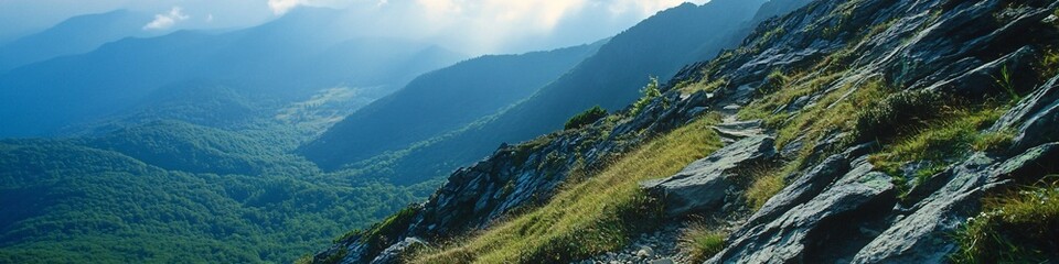 Obraz premium 2410_099.exposed mountain trail traversing rocky slope, multi-colored rock layers, verdant valley below, wispy clouds, rugged wilderness expanse, challenging hiking route
