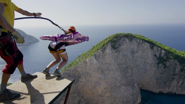 Woman in purple dress bungee jumping off cliff in Greece - cinematic slow motion