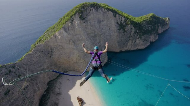 Brave leap off of Greece cliffside over beach, bungee jump in slow motion 