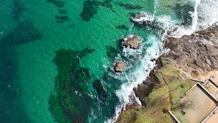 Drone shot aerial view of waves crashing onto rocks near a reef in Australia 