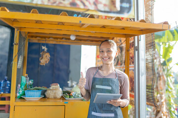 A cheerful vendor stands proudly at her food stall, ready to serve happy customers meals