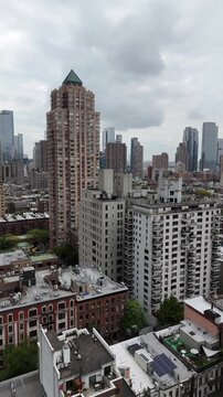 A captivating vertical orientation drone shot of W 52nd Street in New York City, rising and panning to reveal the bustling Manhattan streets, skyscrapers, and dynamic urban environment.