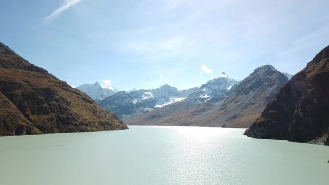 Aerial footage of the Grande Dixence Dam, the tallest gravity dam in the world at 285 meters, with Lac des Dix and snow-capped mountains in the background. Valais, Switzerland, aerial footage