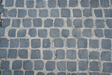 A close-up of light gray cobblestones arranged in a grid pattern. The gaps between the stones are filled with a lighter material, creating a rustic and aged appearance. 