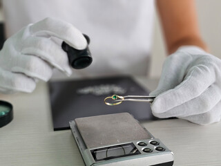 A jeweler examines a gold ring with a green stone using a magnifying glass