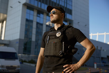 Confident male patrol police officer standing outdoors against police station