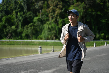 Active young asian man jogging by a riverside path on sunny day
