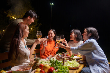 Group of young Asian friends enjoying dinner party together Barbecue grilling, drinking beer, people, food, healthy fruits and vegetables, celebrating, lifestyle drinks. New Year celebration concept.