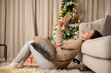 A side view of a happy woman enjoys reading a book in the living room during the Christmas night.