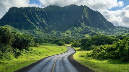 Fototapeta premium Winding country road meandering through vibrant green mountains under a bright blue sky with fluffy clouds.