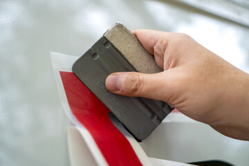 A person installing foil stickers on a car. Applying the sticker with a plastic spatula.