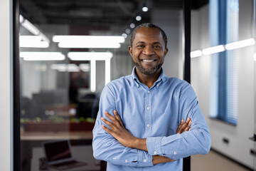 Confident African American businessman standing in modern office. Man wearing blue shirt, smiling...