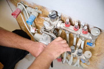 Man adjusting the heating system in a new apartment. Plumber adjusting heat on the central system valves. Service man adjusting house heating system. Underfloor heating system. Crop view