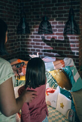Unrecognizable woman and girl having fun together playing in shade show on living room. Back view...